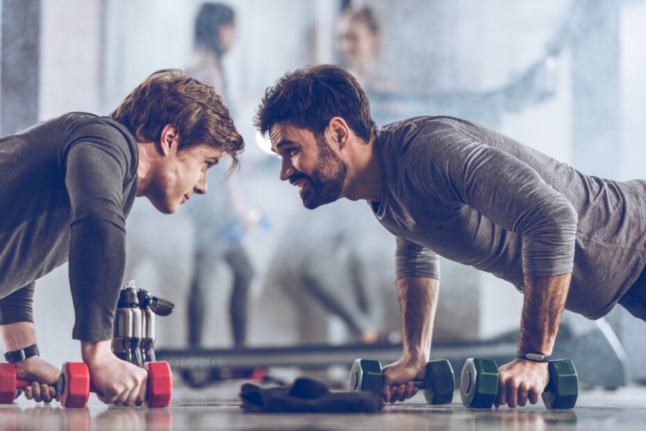 athletic young sportsmen doing push ups with dumbbells at the gym, gym workout concept